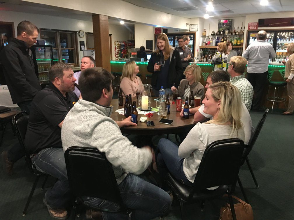 Group of people gathered around a table in the club house with an array of drinks on the table.