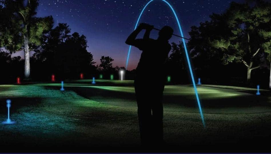 Silhouette of golfer at night. The golf ball arch is shown as a blue line from the golfer to the pin.