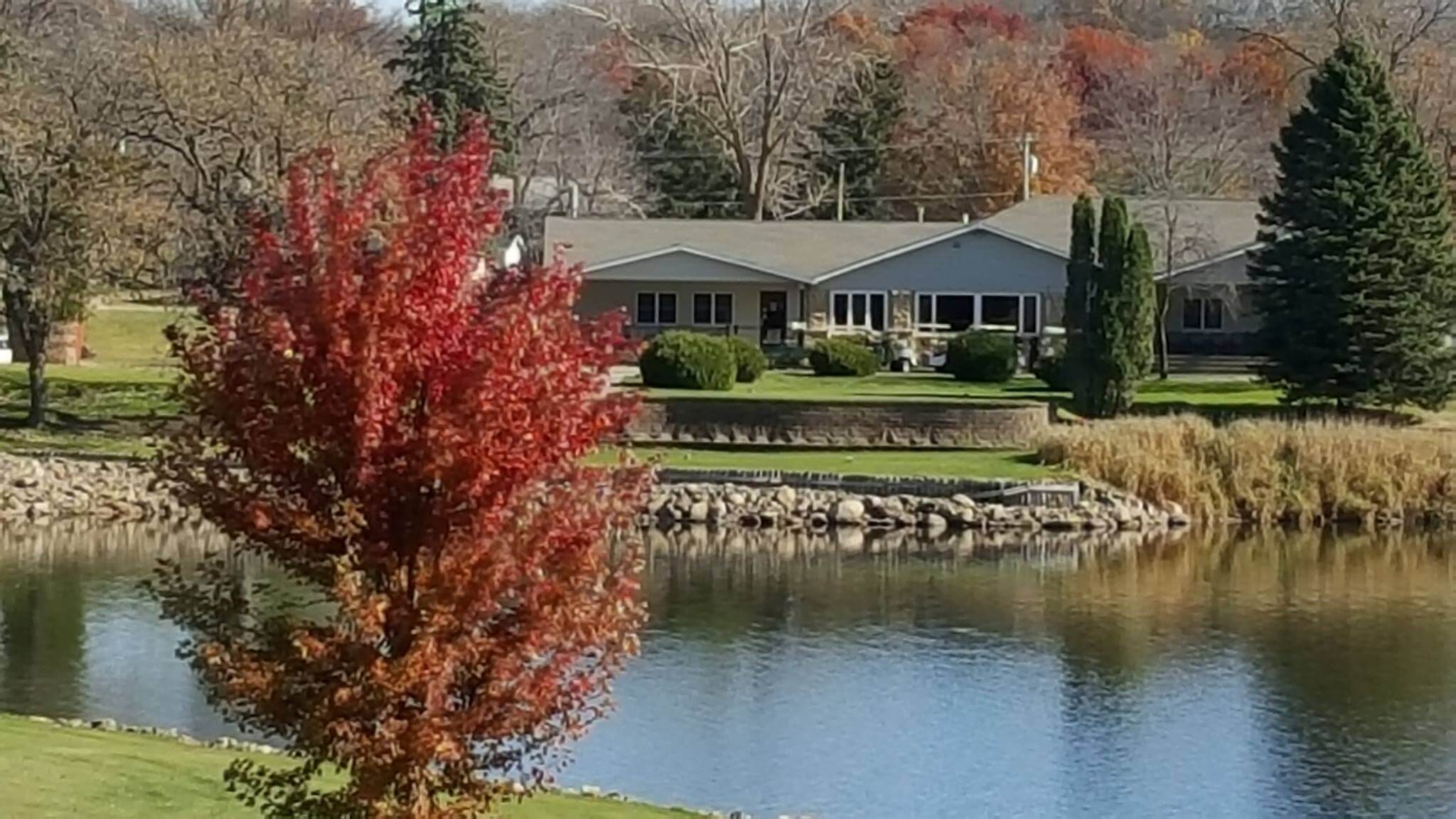 A red autumn tree with a pond and the Cresco Country Club Clubhouse in the background.