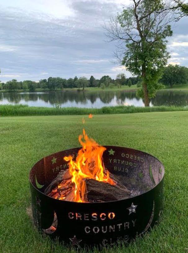 A campfire inside a Cresco Country Club fire ring with a pond in the background. Taken by Don Fenske in June 2020.