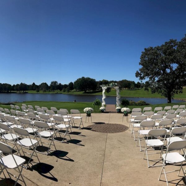 White chairs setup on concrete in front of the pond at Cresco Country Club for a wedding ceremony.