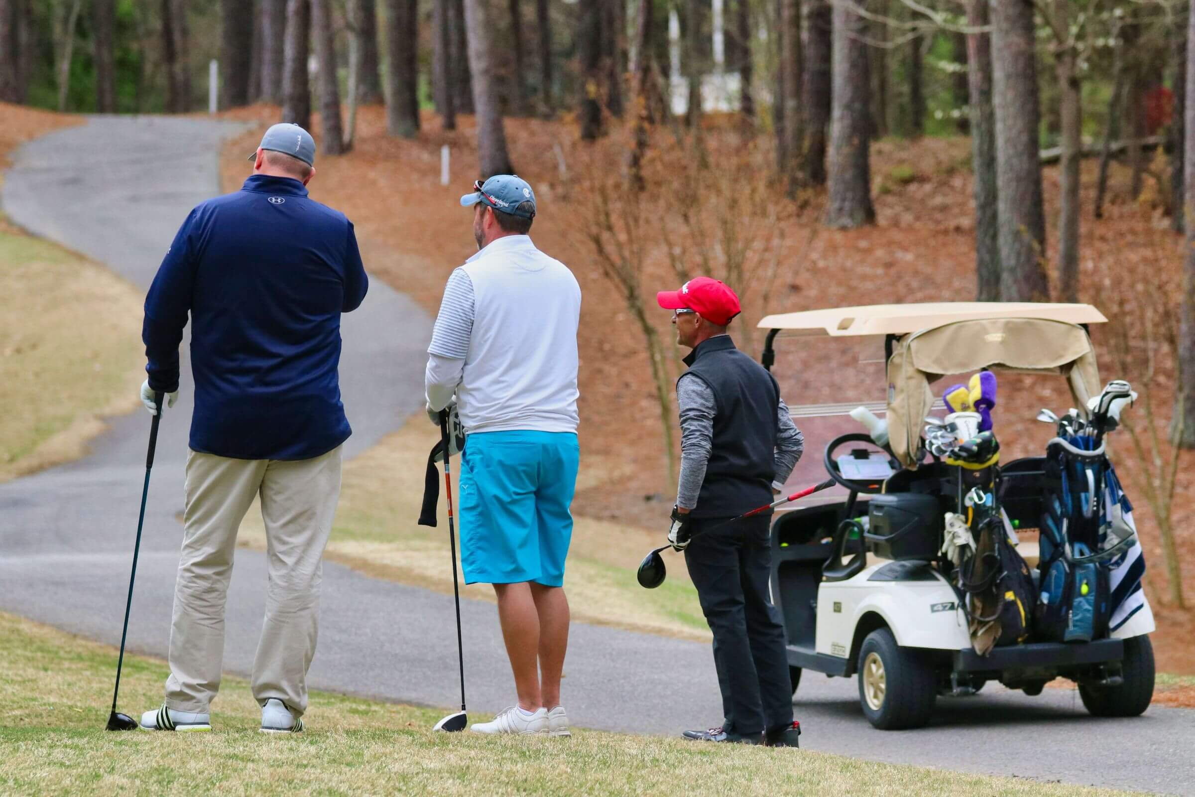 men looking off camera holding golf clubs with golf cart in background