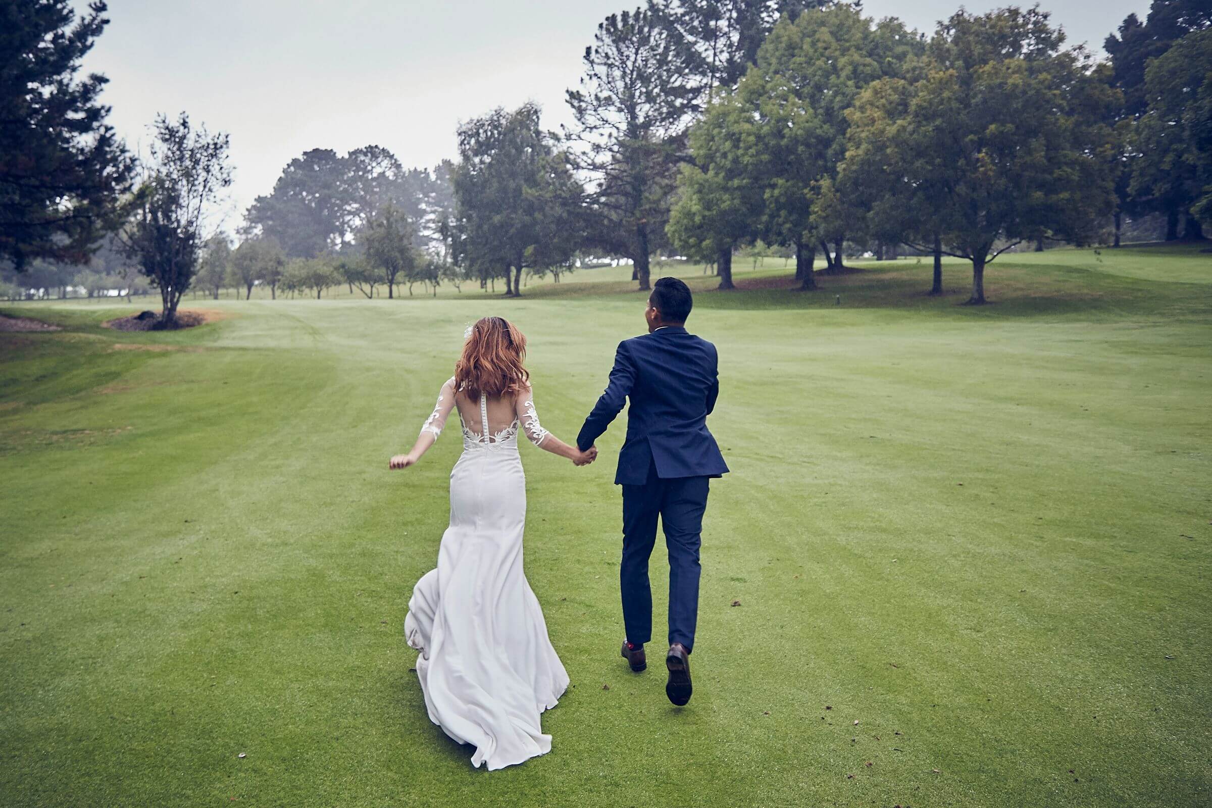 bride and groom from behind running on a golf course